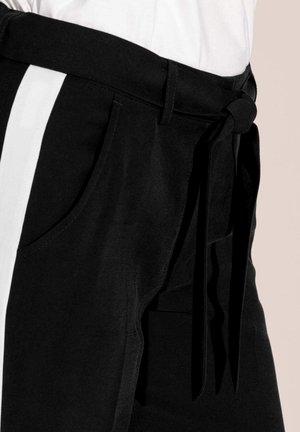 Zwarte broek met een witte verticale streep, voorzien van een strik in de taille, zijzakken en een zachte textuur. Licht getailleerd ontwerp.