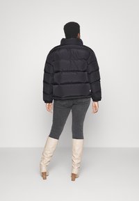 Giubbotto imbottito nero con colletto alto, caratterizzato da una trapuntatura orizzontale. Indossato con pantaloni grigi e stivali crema al ginocchio.
