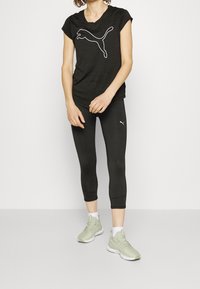 Svart tränings t-shirt med korta ärmar och vit Puma-logotyp, kombinerad med svarta leggings och ljusgröna löparskor, bärs med vita strumpor.