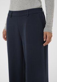 Navy blue wide-leg trousers made of smooth fabric, featuring side pockets and a flat front with a waistband.