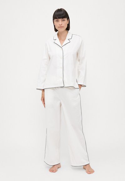Set de pijamale de culoare albă, compus dintr-o bluză cu butoni și tiv negru, mâneci lungi și pantaloni largi cu margine asortată. Textură netedă.