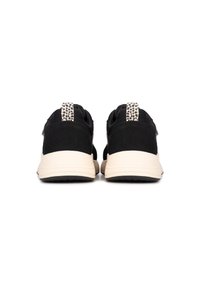 Des chaussures de sport noires avec un design robuste, un dessus noir texturé et des semelles beiges avec une touche émaillée sur l'onglet du talon.