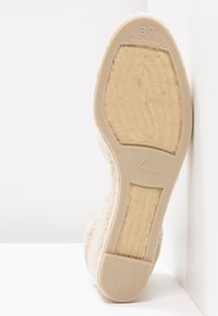 Semelle d'une chaussure compensée espadrille beige montrant la semelle en caoutchouc avec la taille 37, le nom de la marque, et les détails de la semelle intérieure en jute texturée.