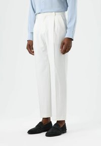 White tailored trousers with pleats, paired with black suede loafers. The fabric has a smooth texture and a straight, tapered cut.