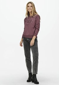 Κάπα σε μπορντώ χρώμα με γράμματα "PARIS", σε συνδυασμό με ξεθωριασμένο γκρι τζιν και μαύρες μπότες μέχρι τον αστράγαλο. Το υλικό φαίνεται μαλακό; ο σχεδιασμός είναι casual και μοντέρνος.