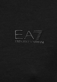 Μαύρο βαμβακερό υφάσμα με ανάγλυφο λογότυπο EA7 Emporio Armani σε κομψή, μεταλλική απόχρωση, τοποθετημένο στο κέντρο για καλύτερη ορατότητα.