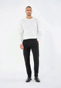 Camicia bianca a maniche lunghe abbinata a pantaloni neri attillati e scarpe nere. La camicia ha un col girocollo, mentre i pantaloni presentano un design classico.