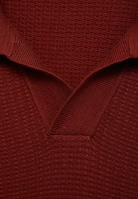 Red knitted sweater with a textured pattern and a V-neck collar. Fabric has a ribbed trim and a soft, warm feel.