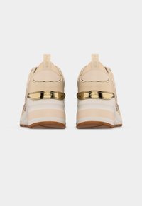 Baskets beiges avec semelles intermédiaires blanches, semelles extérieures marron et accents métalliques dorés sur le talon, vues de dos sur un fond blanc.