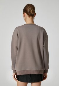 Sweter w kolorze miękkiego taupe, o luźnym kroju z opuszczonymi ramionami, z prążkowanymi mankietami i prążkowanym dołem dla dodatkowej tekstury.