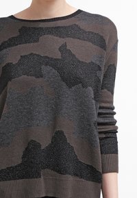 Sweter z dzianiny w odcieniach szarości i brązu, z teksturowanym wzorem kamuflażu. Rybaczane mankiety i dół nadają mu wyrazistości.