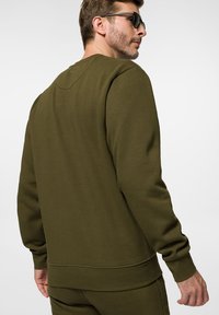 Oliwkowy sweatshirt wykonany z miękkiego materiału, charakteryzujący się okrągłym dekoltem, ściągaczami przy mankietach i na dolnym brzegu oraz luźnym krojem o gładkiej fakturze.