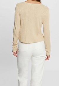 Beige värillinen ribbineuleinen pusero, jossa pitkät hihat, pyöreä pääntie ja kimaltava pinta, yhdistetty valkoisiin korkeavyötäröisiin housuihin, joissa takataskut.