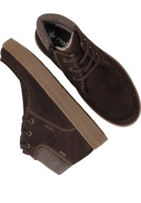 Bottes en daim marron à la cheville avec une semelle en caoutchouc texturée marron, un design à lacets et une doublure douce ressemblant à de la laine. Présente des coutures contrastantes.