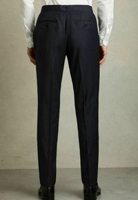 Mørkeblå skræddersyede bukser lavet af tekstureret stof, med to baglommer med knapper og en slim fit design.