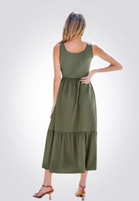 Olijfgroene maxi-jurk met een getailleerd lijfje en een gelaagde rok. Gemaakt van ribbelstof, met een ronde rug en subtiele textuur.
