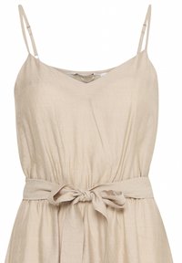 Robe beige sans manches avec fines bretelles et ceinture en tissu nouée en nœud à la taille, avec une taille légèrement froncée.