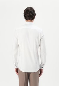 White long-sleeve shirt with a straight cut, buttoned cuffs featuring contrasting color accents, and a smooth texture.