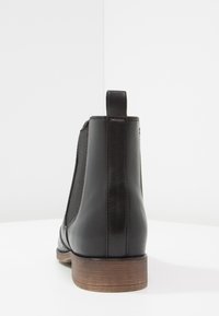 Stivale alla caviglia in pelle nera con pannelli laterali elastici, punta arrotondata e tacco in legno basso e impilato. Presenta un tassello per una facile vestibilità.