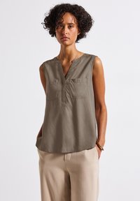 Khaki sans lengan dengan leher v, dua saku depan, dan tekstur halus, dipadukan dengan celana beige. Desain yang sederhana dan santai.