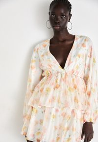 Blusa floral de tejido translúcido, con un profundo escote en V, mangas largas con puños elásticos y un diseño en capas en colores pasteles.