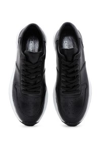 Sneakers in pelle nera con un design con lacci, texture liscia, dettagli perforati sulla punta e suola in gomma bianca.