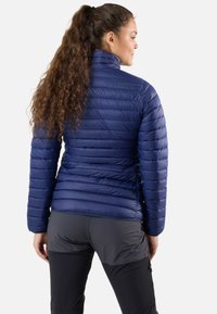 Laivastonsininen puffatakki, jossa on tikattu muotoilu ja korkea kaulus, valmistettu kiiltävästä synteettisestä materiaalista; yhdistetty mustiin ulkoiluhousuihin.