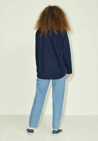 Camicia blu navy con maniche lunghe, dettaglio dei bottoni, abbinata a jeans dritti blu chiaro e scarpe in tela blu navy. Design minimalista.