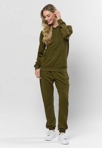 Olíva zöld pulóver és hozzá illő melegítőnadrág szett, puha anyagból készült, elülső zsebbel, húzózsinórral és elasztikus mandzsettákkal.