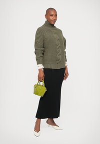 Pulover supradimensionat de culoare verde măsliniu, tricotat, cu guler înalt, asociat cu o fustă neagră cu dungi. Poartă o geantă mică de mână verde lime și pantofi cu toc albi, ascuțiți.