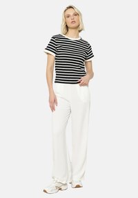 Striped black and white T-shirt with short sleeves, paired with white wide-leg pants and white sneakers featuring a textured sole.