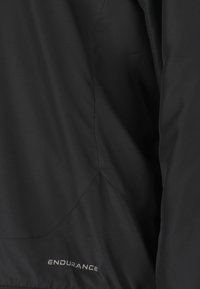 Svart lättviktsjacka i slät tyg, med slim fit, böjda sömmar och ordet "ENDURANCE" tryckt nära fållen.