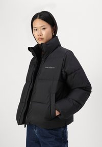 Schwarze Steppjacke mit Reißverschluss, hohem Kragen und einem Logo auf der Brust. Verfügt über elastische Bündchen und Seitentaschen. Stilvolles, gestepptes Design.