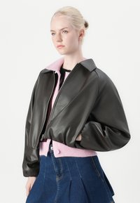 Svart lær cropped jakke med rosa krage, med glidelås foran og vide ermer, kombinert med et denim skjørt.