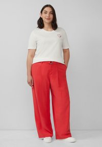 Weißes Kurzarm-T-Shirt mit rotem Herzstick, kombiniert mit lockeren roten Hosen und weißen Sneakers.