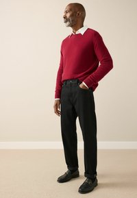 Red knit sweater with a white collar, paired with black trousers and black shoes. The outfit features a relaxed fit and minimal detailing.