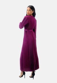 Robe longue plissée violette avec un corsage ajusté et une jupe fluide, dotée de manches longues et d'un détail de taille cintrée.
