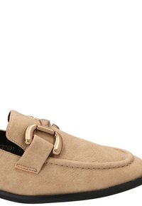 Zapato sin cordones de ante beige con punta redonda, que presenta un acento de hebilla metálica dorada y una suela de goma negra lisa.