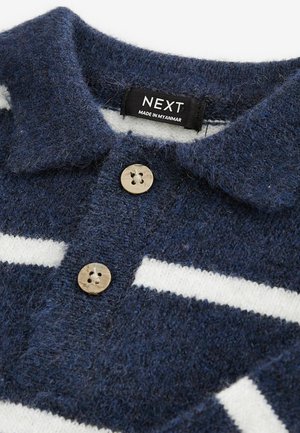 Polo di misto lana blu navy con finitura testurizzata, strisce orizzontali bianche e bottoni beige. L'etichetta riporta "NEXT, Made in Myanmar."