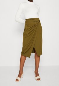 Oliivinvihreä, polven pituinen kietaisuhame, jossa sivulla kiertynyt solmu, valmistettu pehmeästä, joustavasta kankaasta. Yhdistetty valkoiseen poolopaitaan.