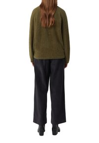 Oliwkowo zielony, puszysty sweter z długimi rękawami, zestawiony z szerokimi czarnymi spodniami. Czarne botki na kostkę dopełniają stylizację, widok od tyłu.