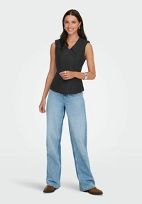 Top senza maniche di un grigio scuro con un design asimmetrico, caratterizzato da un dettaglio con bottone. Abbinato a jeans a gamba larga blu chiaro e scarpe marroni.