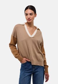 Pull en V beige et marron, avec un col crème contrasté, coupe loose, poignets côtelés et une texture en maille douce.