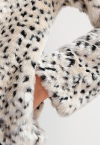 Leopardenmuster Kunstfellstoff mit einer weichen, flauschigen Textur, der schwarze Flecken auf einem beigen Hintergrund zeigt und einen Ärmelbereich präsentiert.