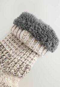 Stricksocken mit einem dicken, grauen, flauschigen Bündchen und einem strukturierten, beige- und cremefarbenen, verflochtenen Muster am Schaft. Weicher, warmer Stoff.