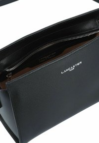 Borsa nera in pelle con una finitura testurizzata, dotata di una chiusura con cerniera e accessori in argento. Interno etichettato "made in France."