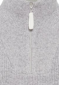 Grijze gebreide pullover met een hoge kraag, voorzien van een halve rits en een zachte textuur. Het ribbelontwerp verhoogt de visuele interesse.