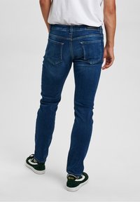 Smal passform blå denimjeans med medelhög midja, bakfickor och en subtil sliten struktur. Styled med svart och vita sneakers.