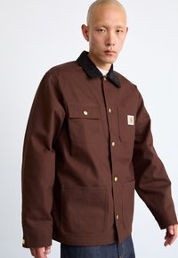 Brown work jacket with a black corduroy collar, featuring gold buttons, two chest pockets, and a logo patch on the left side.