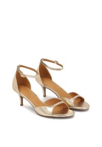Sandales à talons hauts en métal doré avec des fines lanières autour de la cheville, design à bout ouvert, surface texturée et un élégant talon aiguille.